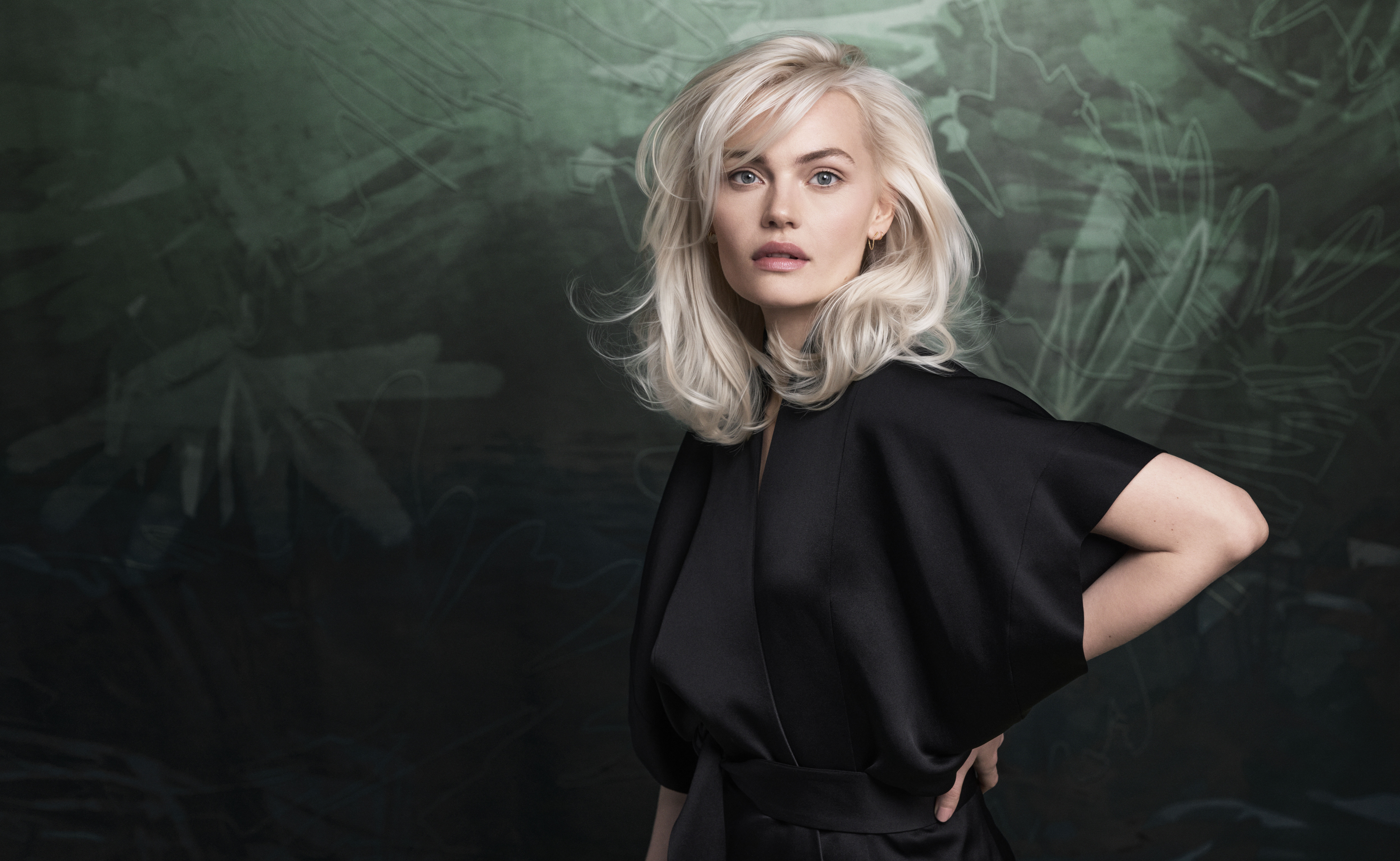 - Spa Bleü in West Dundee, St. Charles and South Barrington, IL A woman with platinum blonde hair wearing a black outfit stands in front of a dark green, abstract background, looking directly at the camera. - Spa Bleü in West Dundee, St. Charles and South Barrington, IL