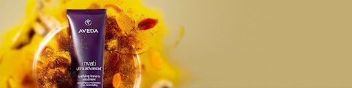Aveda Invati Advanced hair treatment tube is displayed in front of a yellow background with flower petals and spices—perfect for holiday hair prep and festive hair ideas. - Spa Bleü in West Dundee, St. Charles and South Barrington, IL