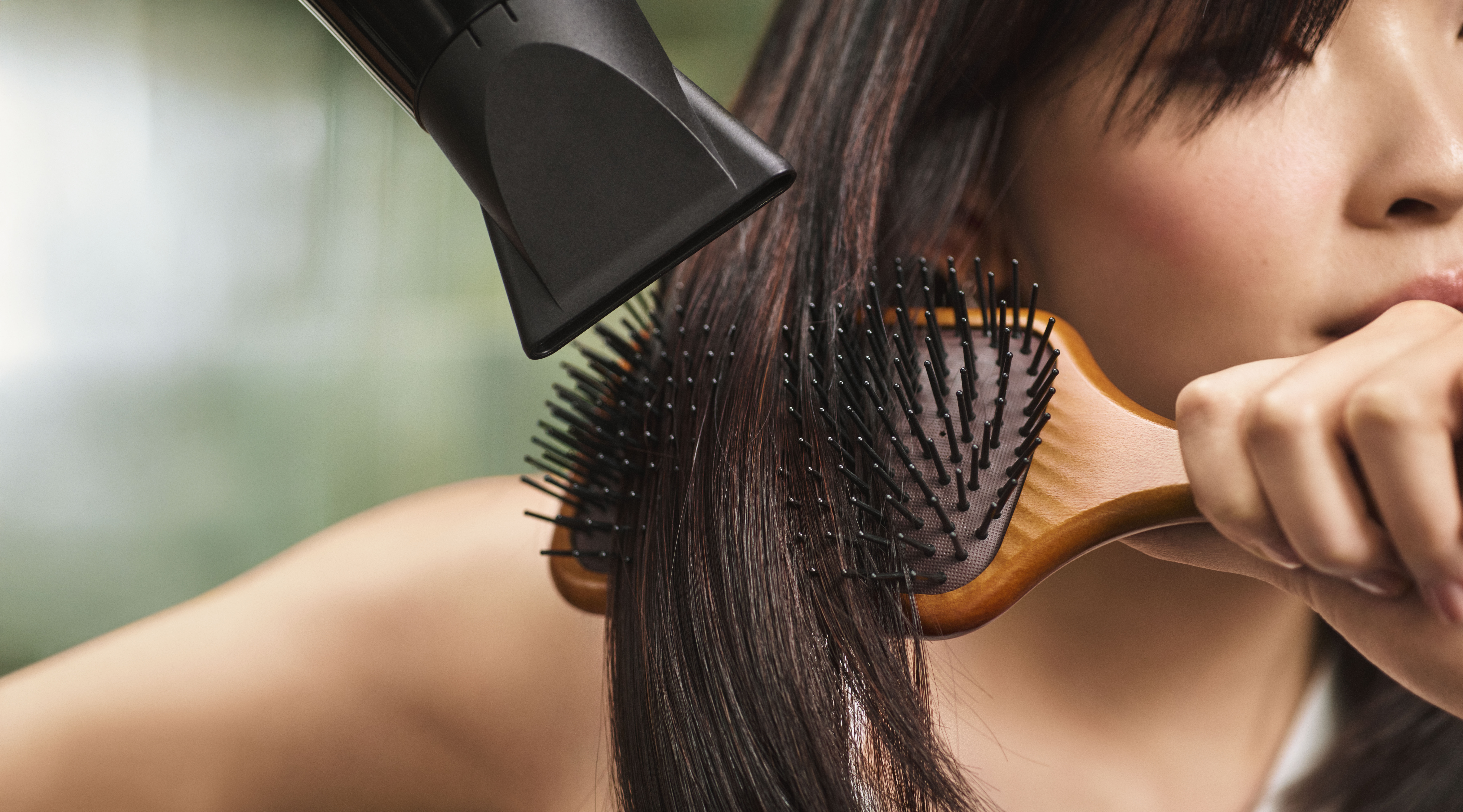 A person blow-drying their straight, dark hair with a hair dryer while brushing it with a paddle brush. - Get Panache, FL